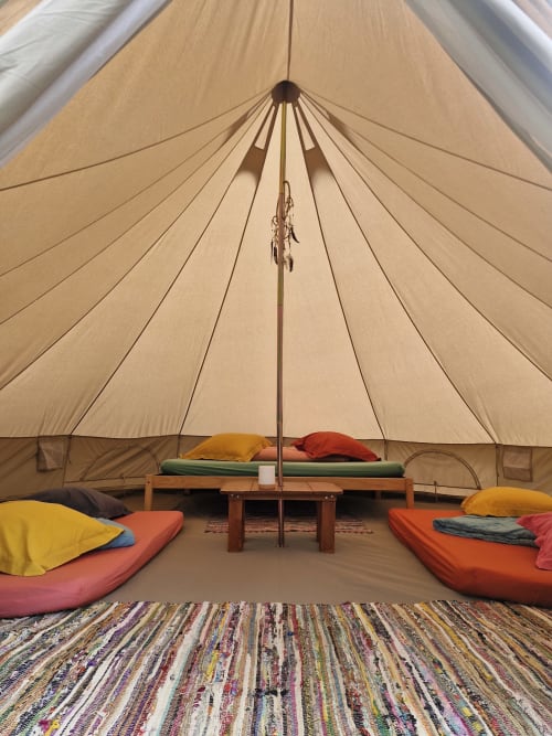 Intérieur spacieux de tente lodge à La Petite Ferme avec matelas colorés, oreillers, table en bois et tapis rayé