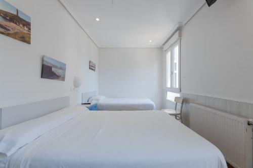 Habitación doble limpia en Hostal Costa Coruña con ropa de cama blanca, TV y vistas a la ciudad de A Coruña