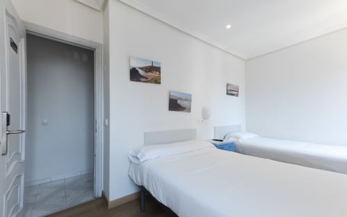 Habitación doble limpia en Hostal Costa Coruña con dos camas individuales, sábanas blancas, TV mural y vistas al mar
