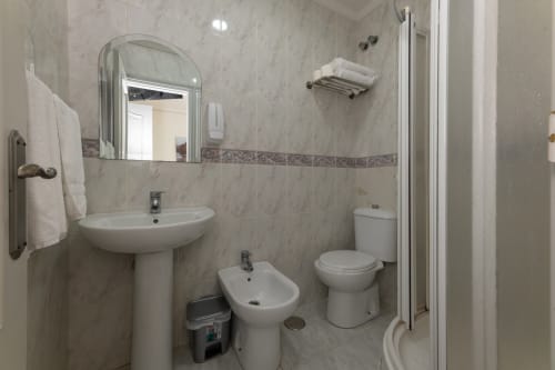 Baño moderno con lavabo blanco, bidé, inodoro y ducha en el Hostal Costa Coruña, A Coruña