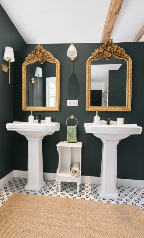 Salle de bains élégante avec double vasque sur piédestals à Bastide la Mourelette, murs vert foncé, miroirs dorés ornementés et carrelage à motifs