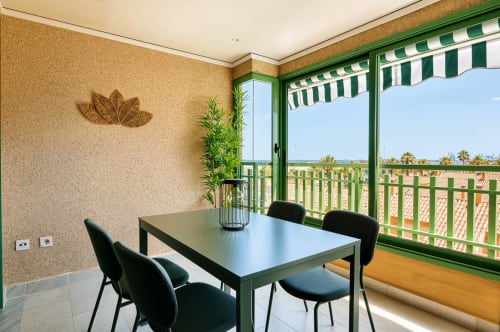 Comedor moderno con balcón con vista al mar sobre la playa de Valencia, toldo de rayas verdes, paredes de corcho, sillas negras