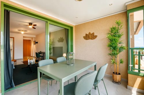 Zona de comedor moderno con vistas al mar en apartamento de Valencia, marcos verdes, sillas azul claro, planta en maceta