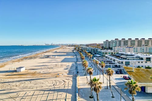 Edificio de apartamentos frente al mar en Valencia con paseo arbolado de palmeras, playa de arena y vistas al mar Mediterráneo