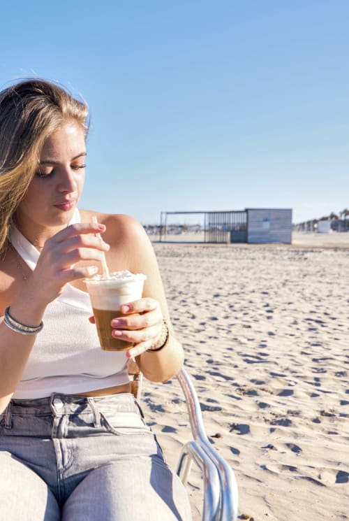 Mujer disfrutando de una bebida en la playa cerca de apartamento en Valencia con vistas al mar e instalaciones de playa