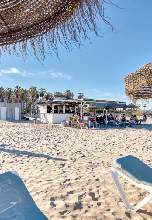 Chiringuito de playa con sombrillas blancas, palmeras y zona de comedor en Pataconablue Rentals, Valencia