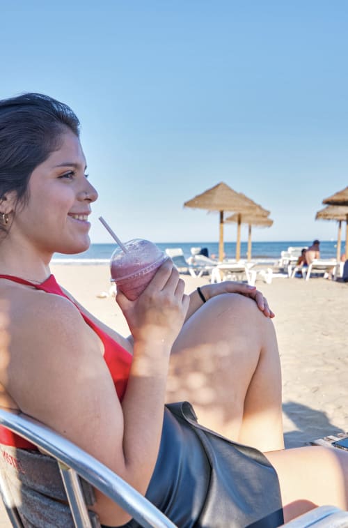 Mujer disfrutando de una bebida refrescante en la playa de Valencia cerca de Pataconablue Rentals con sombrillas y vista al mar