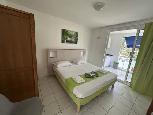 Monolocale moderno alle Créolines con letto matrimoniale, dettagli verdi, balcone con vista piscina e angolo cottura completo