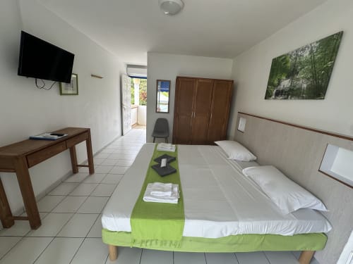 Camera studio dell'hotel Les Créolines a Sainte-Luce con letti gemelli, TV, scrivania e dettagli verdi