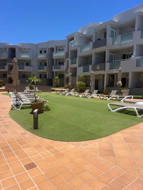 Patio de FTV Holidays Homes en Corralejo con tumbonas, palmeras y modernos edificios blancos bajo cielo azul