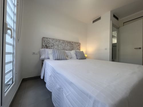 Dormitorio moderno con sábanas blancas, almohadas rayadas y cabecero decorativo en FTV Holidays Homes de Corralejo