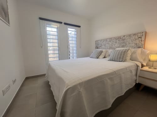 Luminoso dormitorio en FTV Holidays Homes Corralejo con cama matrimonial, almohadas a rayas, cabecero tejido y puertas al balcón