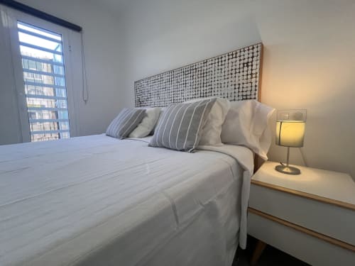 Dormitorio moderno en apartamento de Corralejo con cama doble, almohadas rayadas, cabecero geométrico y lámpara de noche
