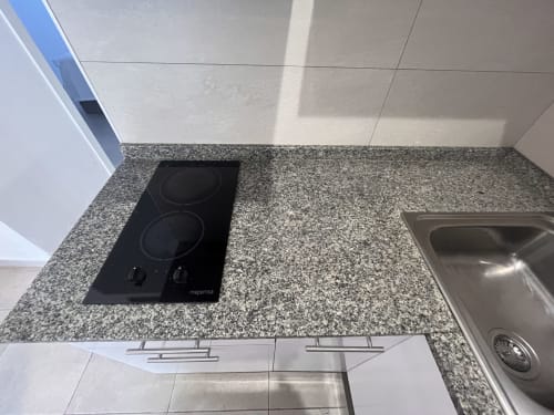 Encimera moderna de cocina con placa vitrocerámica negra y fregadero de acero inoxidable en apartamento de Corralejo