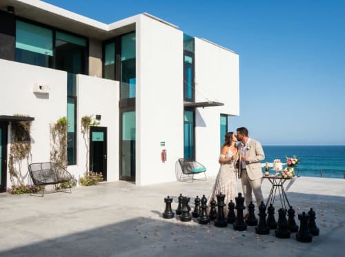 Pareja elegante en la propiedad frente al mar Vidasoul en La Vinorama, México, con ajedrez gigante y vista al océano.