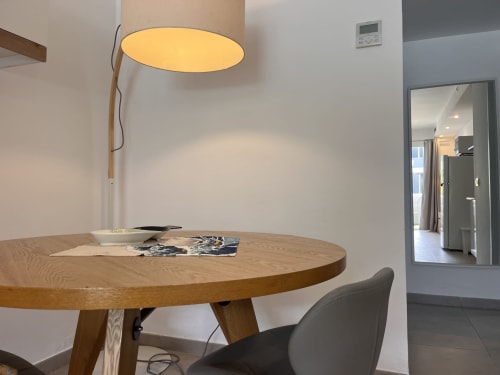 Zona de comedor moderna en apartamento de Corralejo con mesa redonda de madera, lámpara colgante amarilla y acceso a cocina