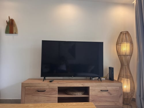 Sala moderna con televisor de pantalla plana en mueble de madera, lámpara de pie tejida y decoración minimalista en apartamento de Corralejo