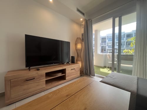 Sala de estar moderna con Smart TV, muebles de madera y balcón con vistas a Corralejo en FTV Holidays Homes