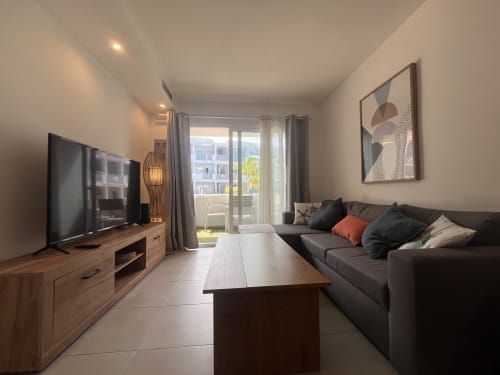 Moderno salón en Corralejo con sofá oscuro, mueble de televisión de madera y vistas a la terraza en FTV Holidays Homes