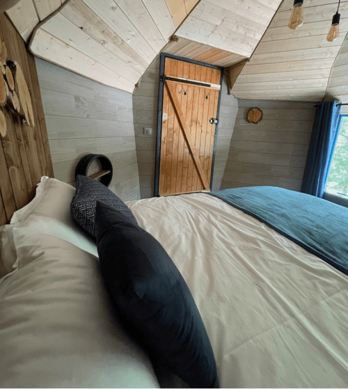 Person relaxing on bed in Nuit Céleste room at Les Murmures du Bois, French countryside B&B with wooden beams and garden view