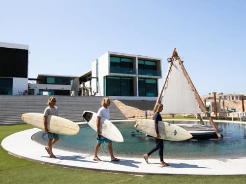 Surfistas cargando tablas en la playa Vidasoul del resort La Vinorama, México, con arquitectura moderna y piscina laguna