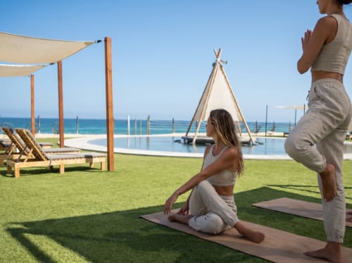 Dos mujeres practicando yoga en el pasto del retiro beachfront Vidasoul en La Vinorama, México, con vista al océano y tipi