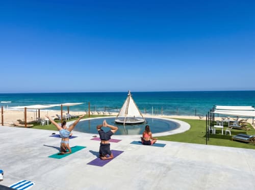 Tres huéspedes practicando yoga en la terraza frente al océano de Vidasoul en La Vinorama, México, con vista a la piscina y la playa