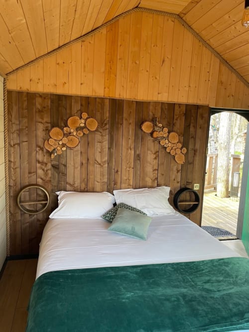 Cozy wooden cabin bedroom at Les Murmures du Bois with queen bed, white linens, and wood-slice wall art decoration