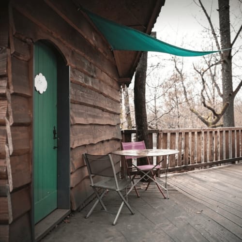 Wooden cabin patio at Les Murmures du Bois with green door, table, chairs, and teal awning overlooking bare trees