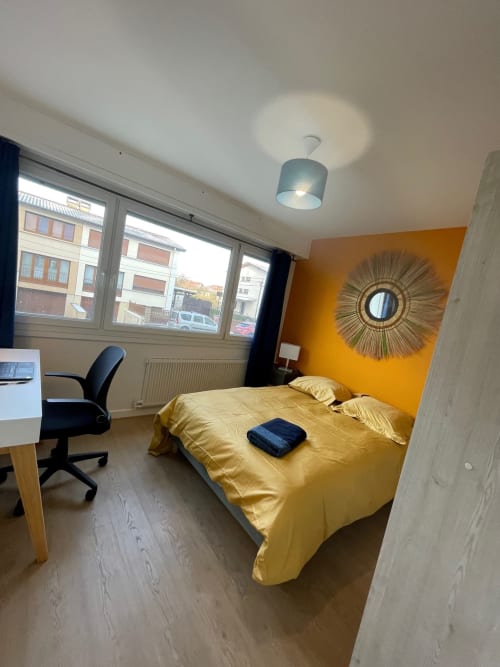 Bright yellow bedroom at Mattbnb Metz with gold bedding, work desk, and city views through windows