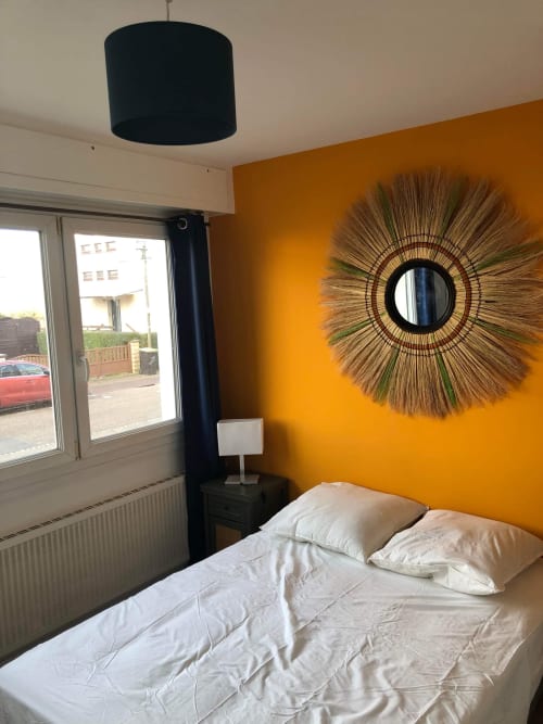 Chambre jaune éclatante chez Mattbnb Metz avec lit, miroir soleil décoratif, suspension noire et vue sur la ville