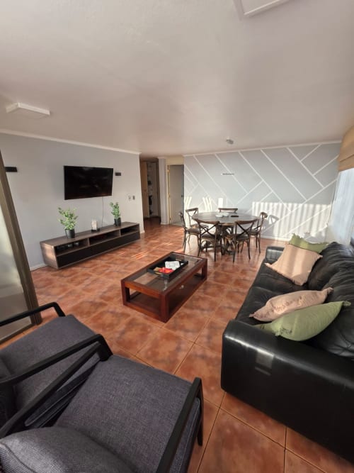 Sala moderna de Your Place Spa, Antofagasta con sofá de cuero negro, TV, comedor y piso de terracota