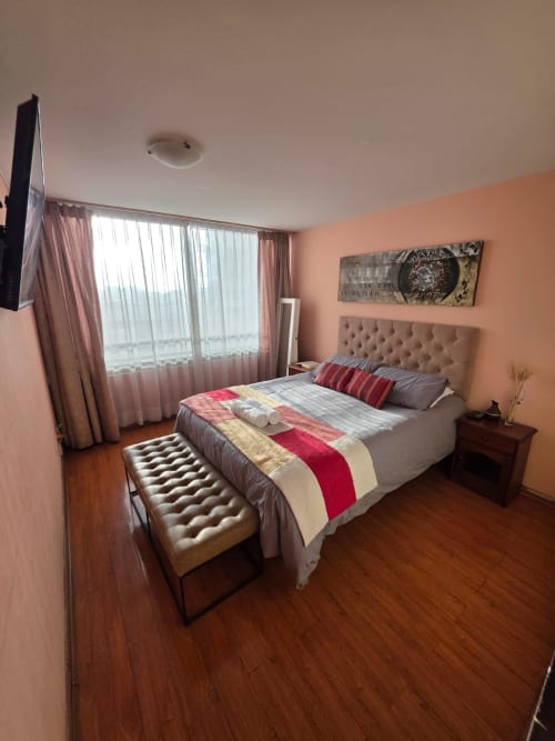 Amplio dormitorio con paredes color durazno, cama queen, vista al mar por grandes ventanales, TV y pisos de madera en hotel Your Place Spa