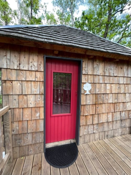 Wooden cabin entrance with red door at Les Murmures du Bois, a French countryside bed and breakfast retreat