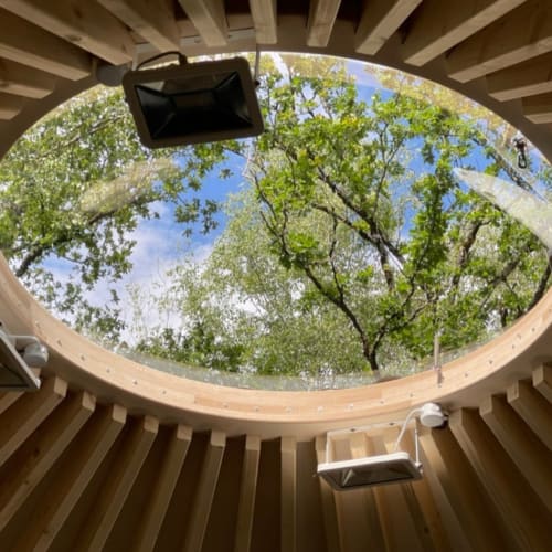 Circular skylight with wooden beams framing lush green tree canopy at Les Murmures du Bois garden view room