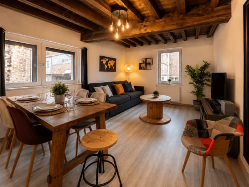Appartement cosy à la Chambres d'hôtes Systeo à Châtillon-sur-Chalaronne avec poutres en bois, table à manger, canapé noir et vue sur la ville