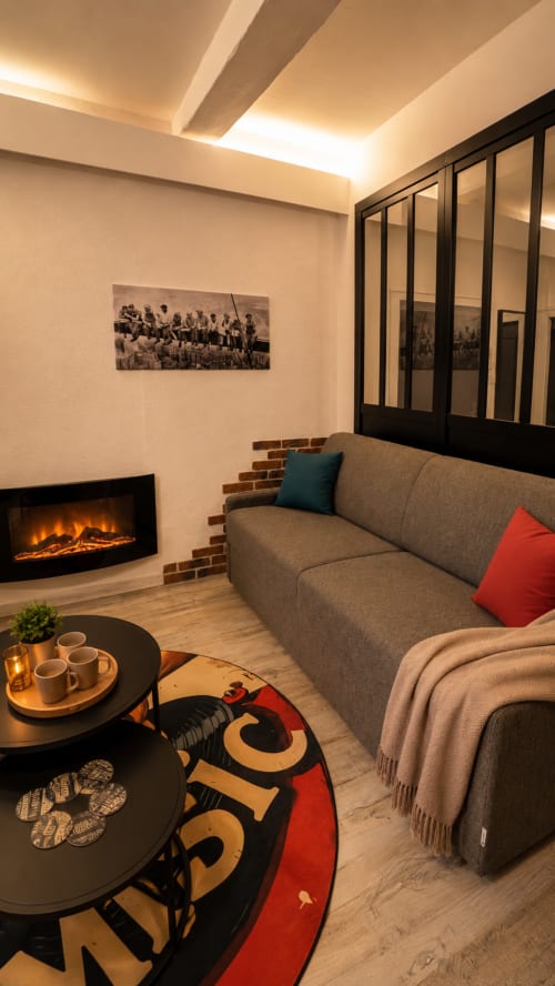 Salon moderne de l'appartement Systeo à Mâcon avec canapé gris, cheminée électrique et verrière noire