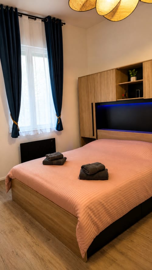 Chambre moderne à Systeo Mâcon avec lit queen-size, literie rose, mobilier en bois, TV écran plat et vue sur la ville
