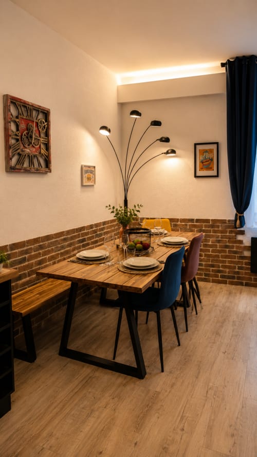 Salle à manger moderne Systeo Mâcon : table en bois, chaises noires, murs en brique, lampadaire arc et tableaux encadrés