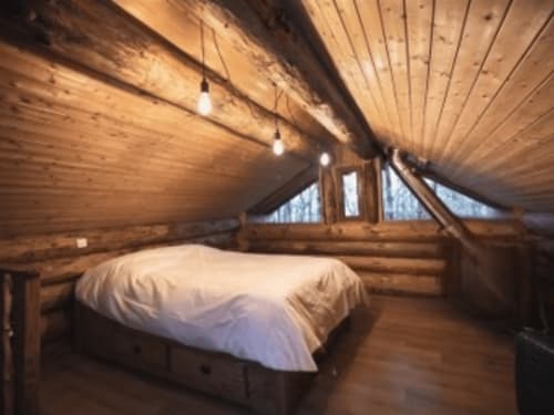 Cozy wooden loft bedroom at Les Murmures du Bois with white bedding, exposed beams, pendant lights, and triangular windows