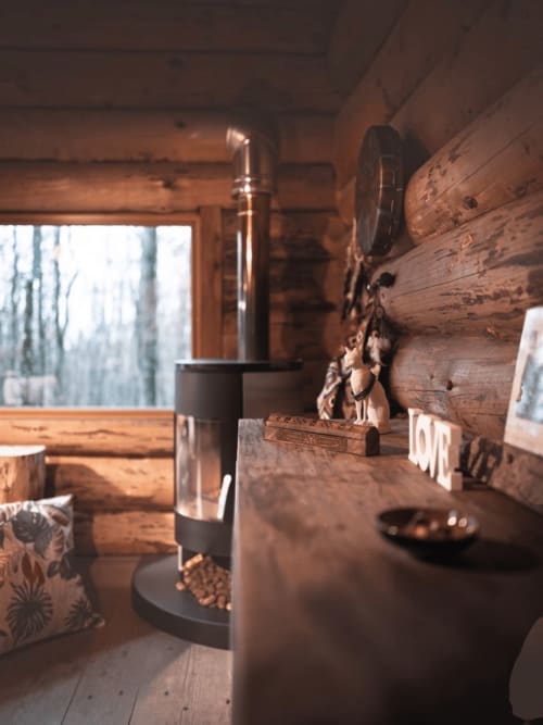 Rustic log cabin interior at Les Murmures du Bois with wooden beams, modern stove, and garden view