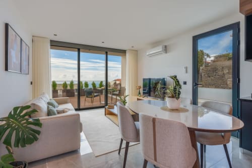 Interior moderno da villa com vista para o oceano, mesa de jantar, assentos confortáveis e acesso ao terraço em BHF Residences Arco da