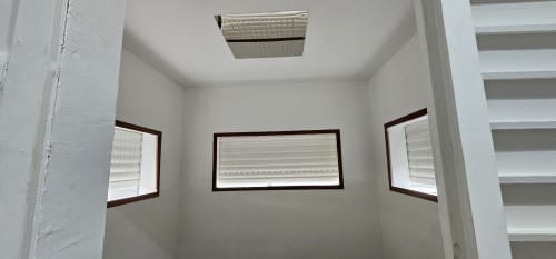 Chambre intérieure lumineuse avec trois fenêtres et ventilation au plafond du bungalow Habitation Villa Les Cassias à Petit