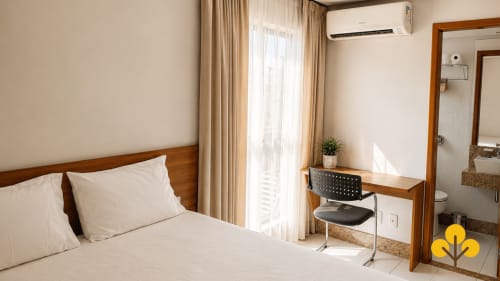 Quarto moderno do Hotel Wellington Rodovalho em Goiânia com cama de madeira, secretária e vista da cidade da varanda