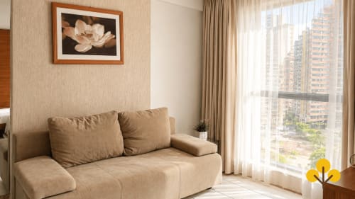 Sofá bege em apartamento moderno em Goiânia com vista da cidade, obras de arte emolduradas e janelas do piso ao teto