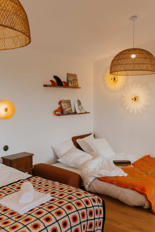 Chambre confortable aux écuries du bout du monde avec luminaires suspendus tissés, literie blanche, touches orangées et étagères en bois