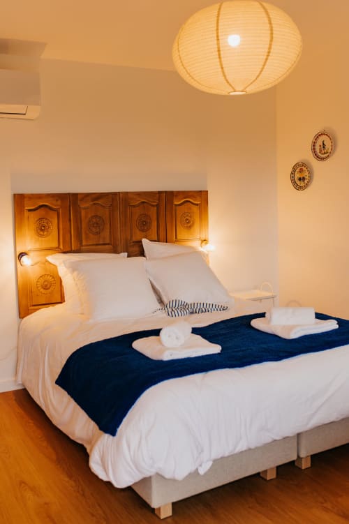 Chambre douillette aux écuries du bout du monde avec tête de lit en bois, literie blanche, jeté bleu marine et lanterne en papier au plafond