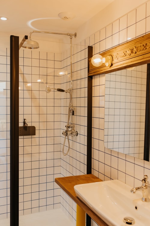 Salle de bains moderne avec carrelage métro blanc, douche pluie, meuble de salle de bains en bois et accessoires en laiton aux Écuries du bout du monde