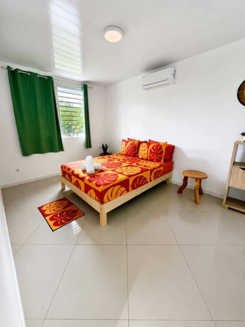 Chambre de lodge tropical lumineuse avec literie à motifs rouge et jaune, lit en bois, rideaux verts et climatisation