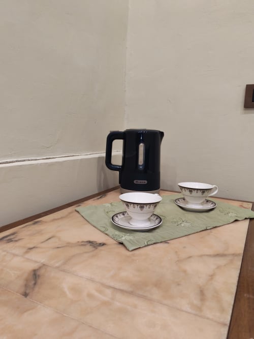 Bollitore elettrico nero e tazze da tè decorative su tavolo in marmo presso l'hotel Sicily Confort Maison a Linguaglossa